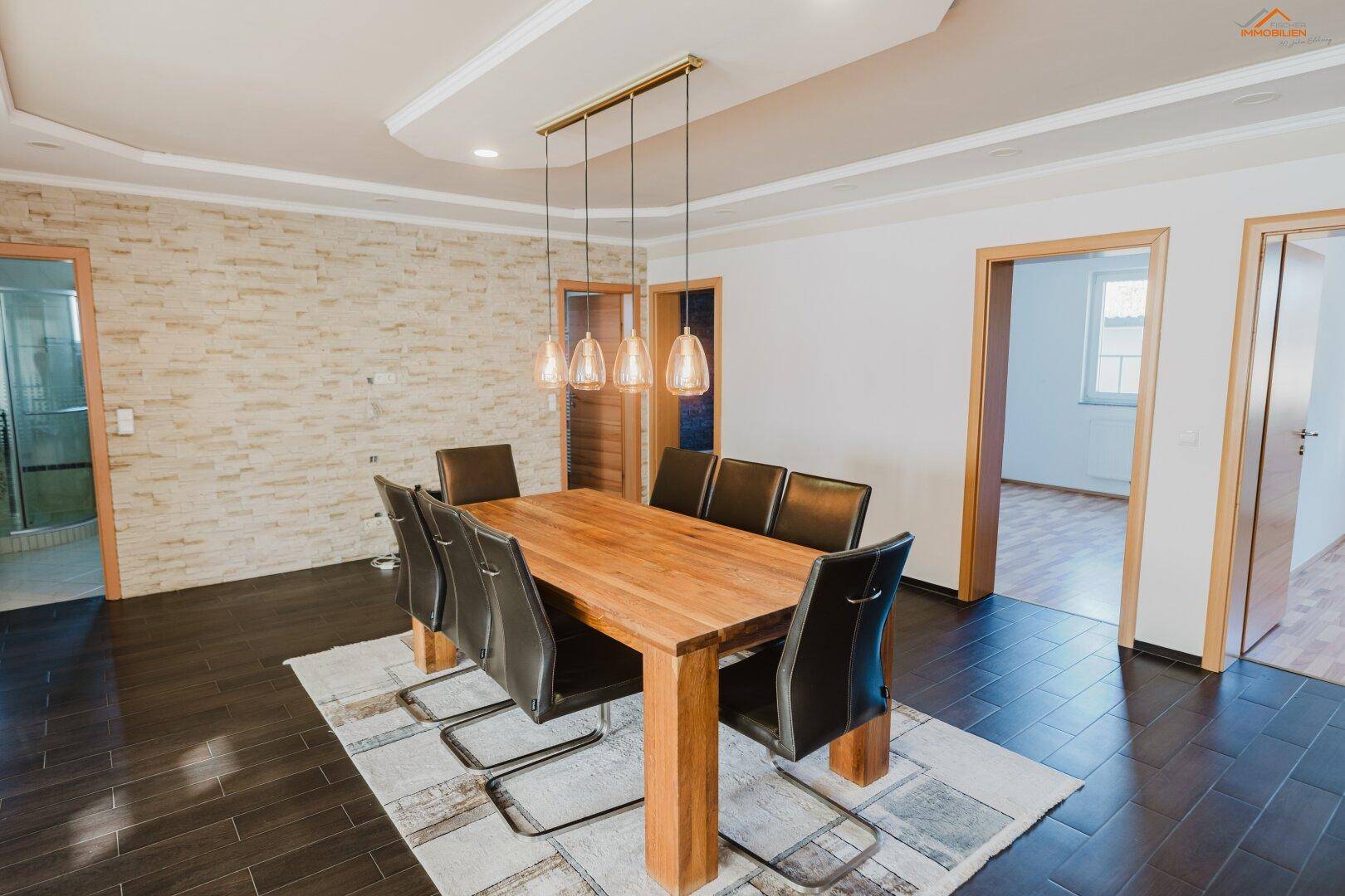 Geräumiger Essbereich mit Holztisch, dunklen Stühlen und dekorativer Steinwand.