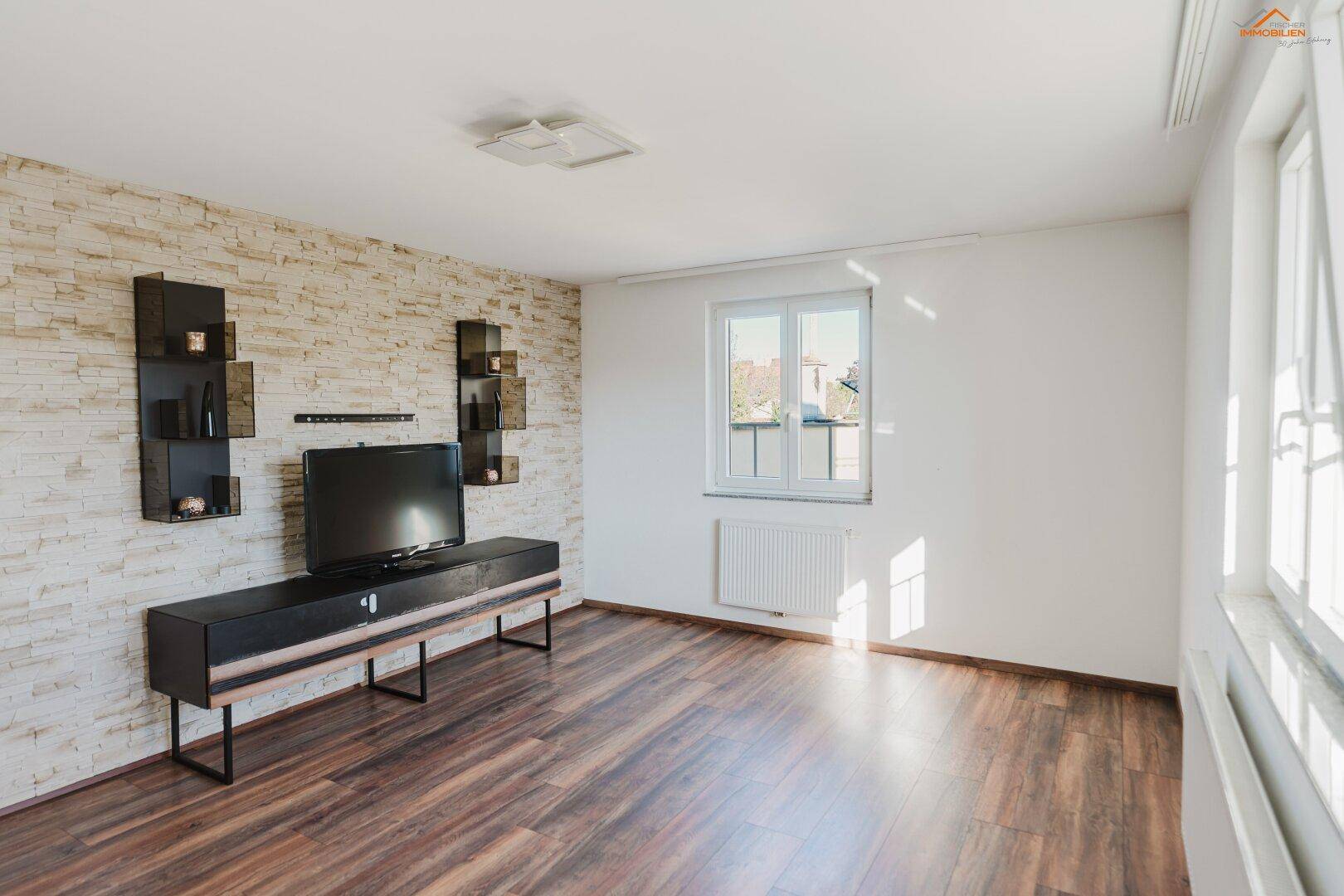 Helles Wohnzimmer mit Holzboden, Steinwand und moderner TV-Möbelkombination.