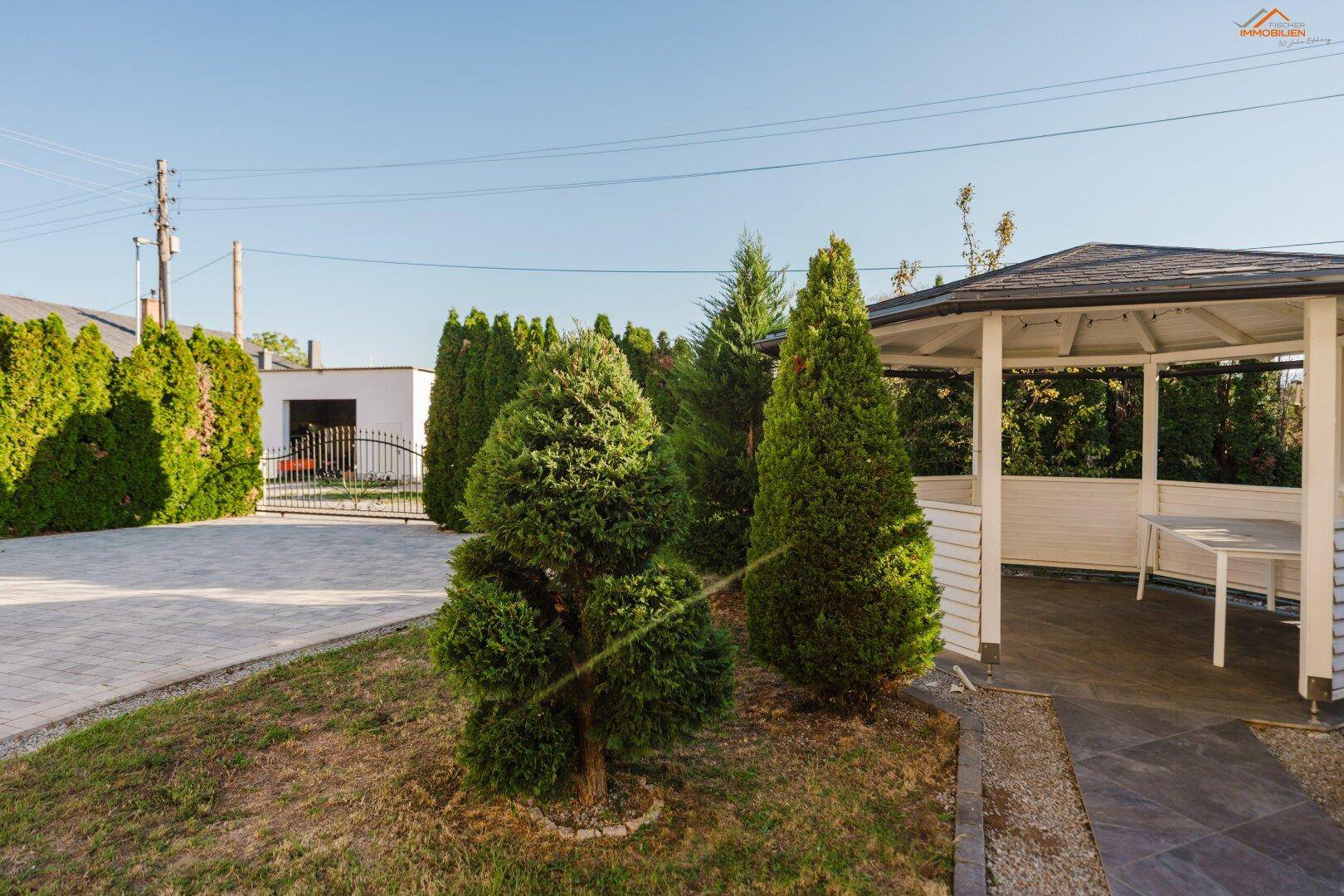 Gepflegter Gartenbereich mit einem Pavillon, Zierbäumen und einer gepflasterten Fläche.