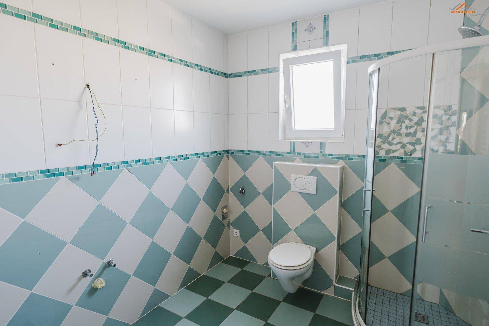Badezimmer mit Duschkabine, Wand-WC und auffälligen blau-weißen Fliesenmustern.