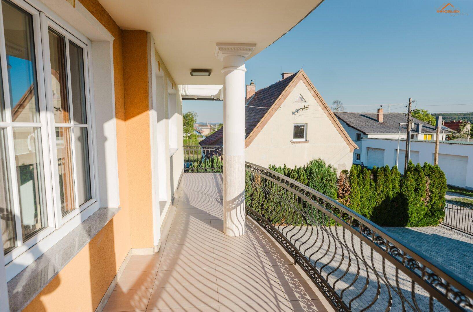 Überdachter Balkon mit Säulen und schmiedeeisernem Geländer, bietet einen Blick auf die Umgebung.
