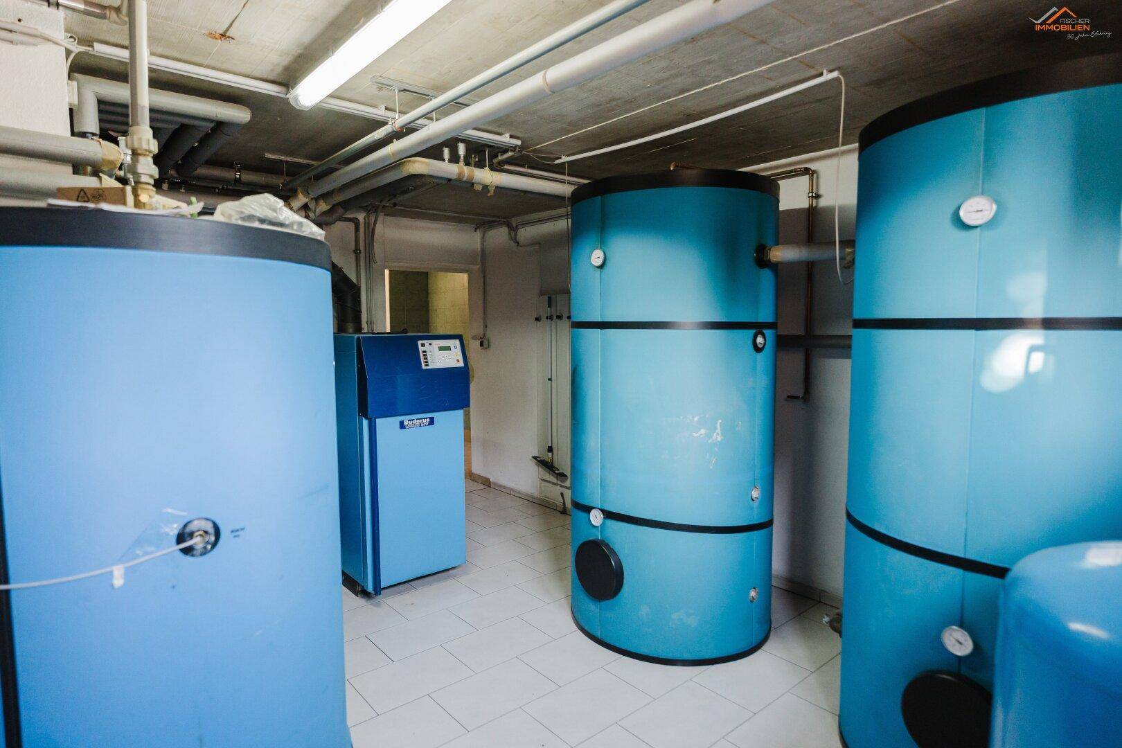 Heizungsraum mit mehreren großen blauen Warmwasserspeichern und sichtbaren Rohrleitungen.