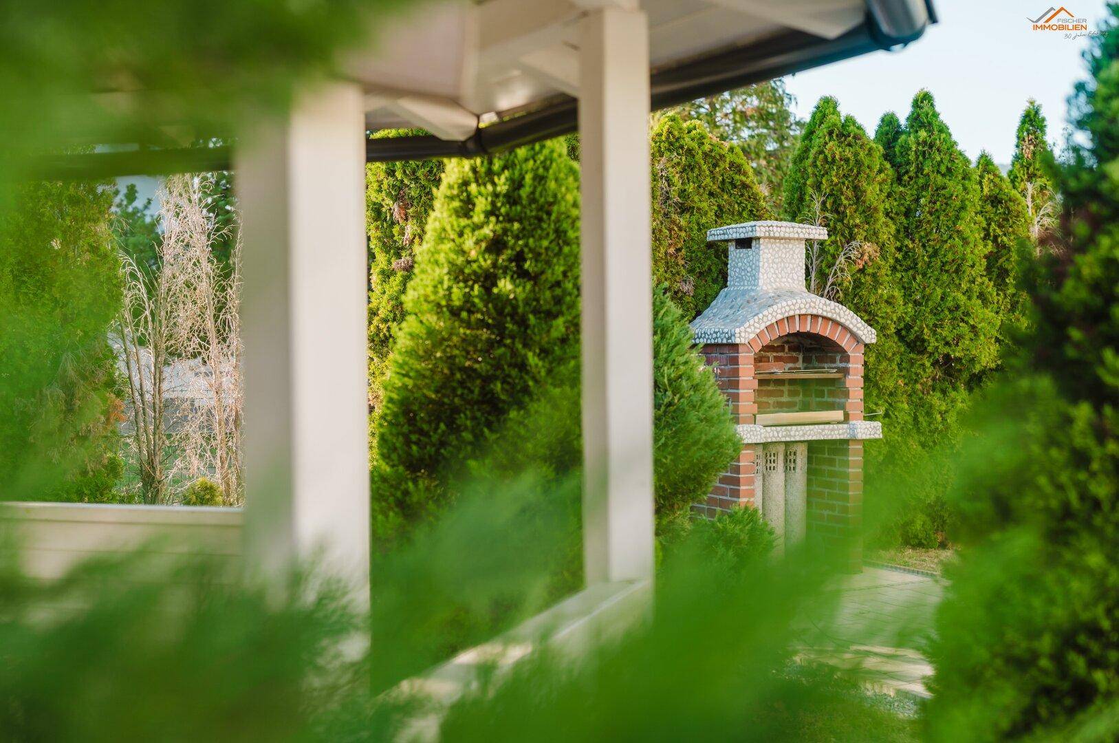 Gemütlicher Gartenbereich mit einem gemauerten Grill und hohen Hecken für Privatsphäre.