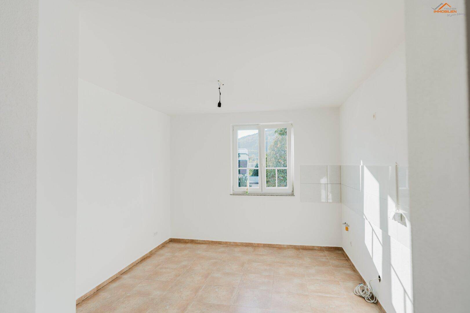 Leerer Küchenraum mit Fliesenboden und vorbereiteten Anschlüssen für eine Einbauküche.