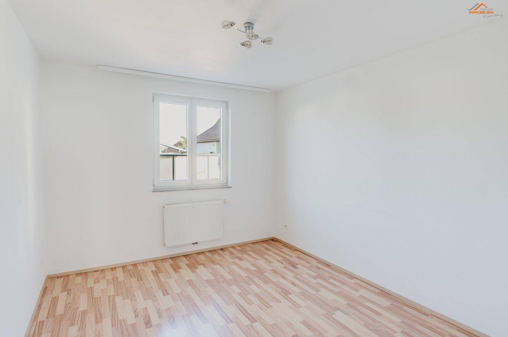 Helles Schlafzimmer mit Holzboden und großem Fenster, das viel Tageslicht hereinlässt.