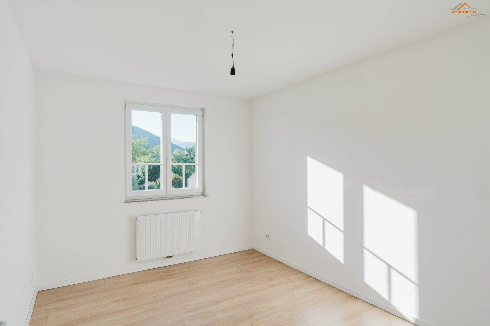 Helles Schlafzimmer mit hellem Holzboden und Fenster mit Blick ins Grüne.