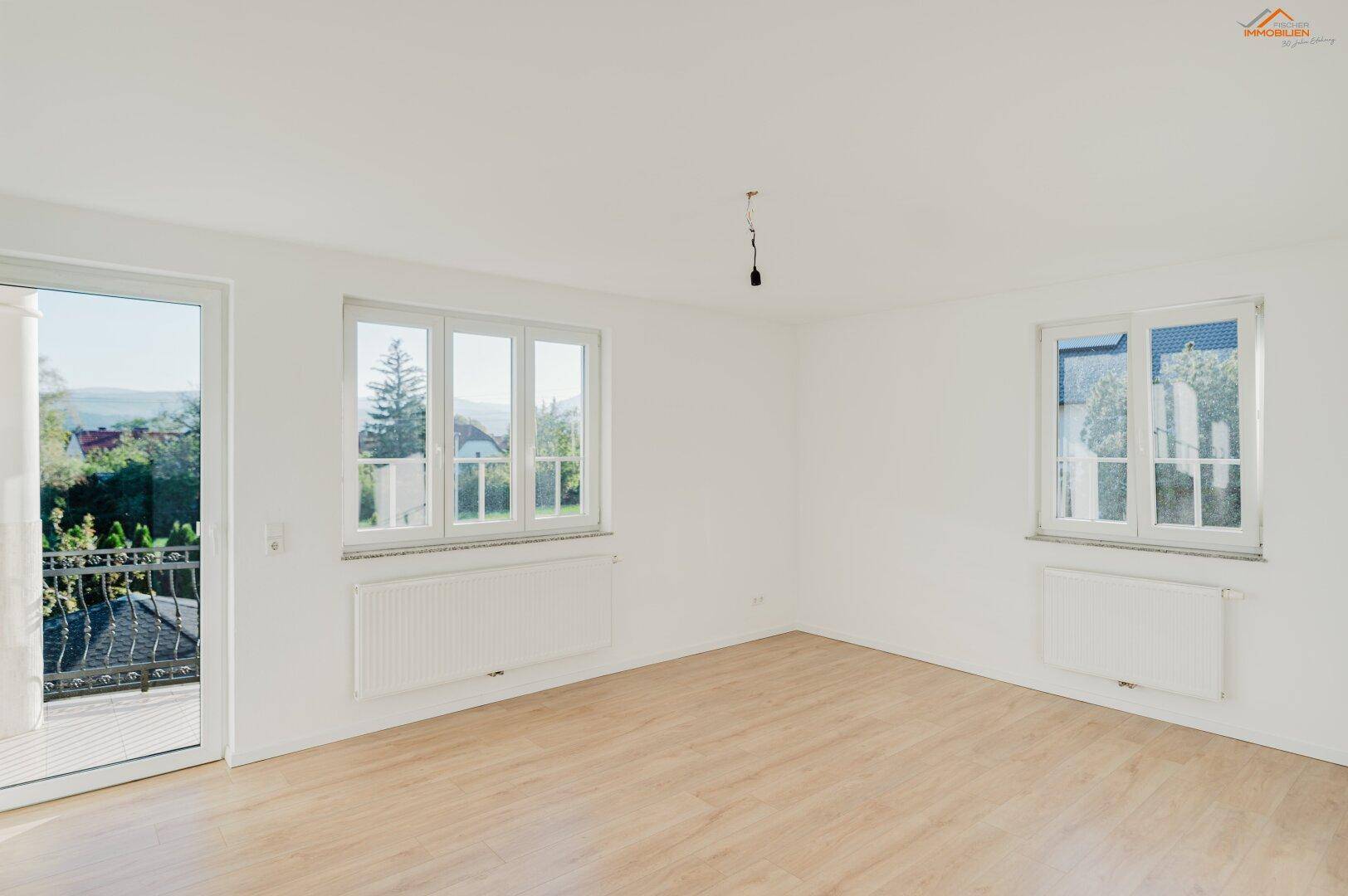 Heller Wohnraum mit Holzboden, großen Fenstern und direktem Zugang zum Balkon.