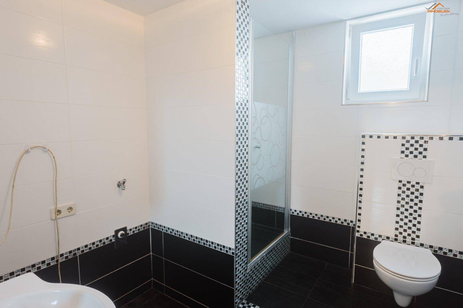 Modern gefliestes Badezimmer in Schwarz-Weiß mit Duschkabine und wandhängendem WC.
