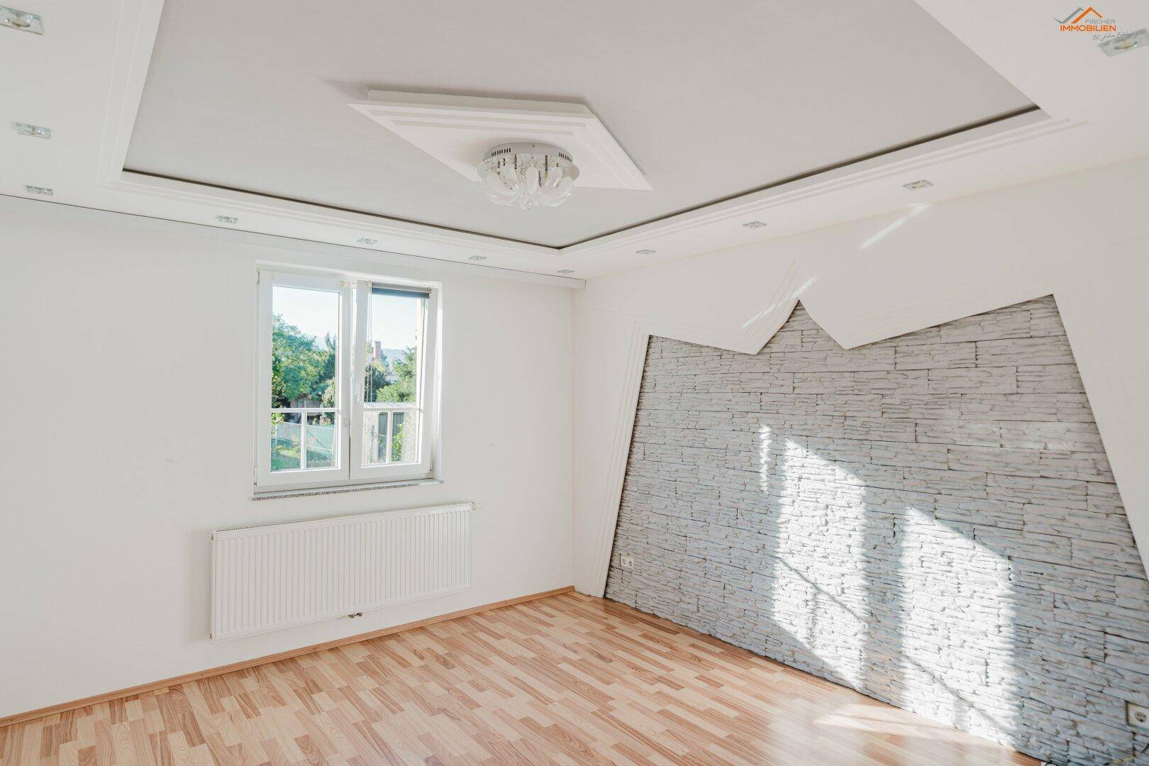 Helles Schlafzimmer mit Holzboden, dekorativer Steinwand und indirekter Deckenbeleuchtung.