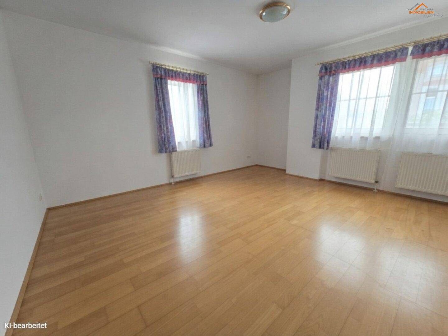 Geräumiges Wohnzimmer mit zwei Fenstern, Parkettboden und Heizkörpern.