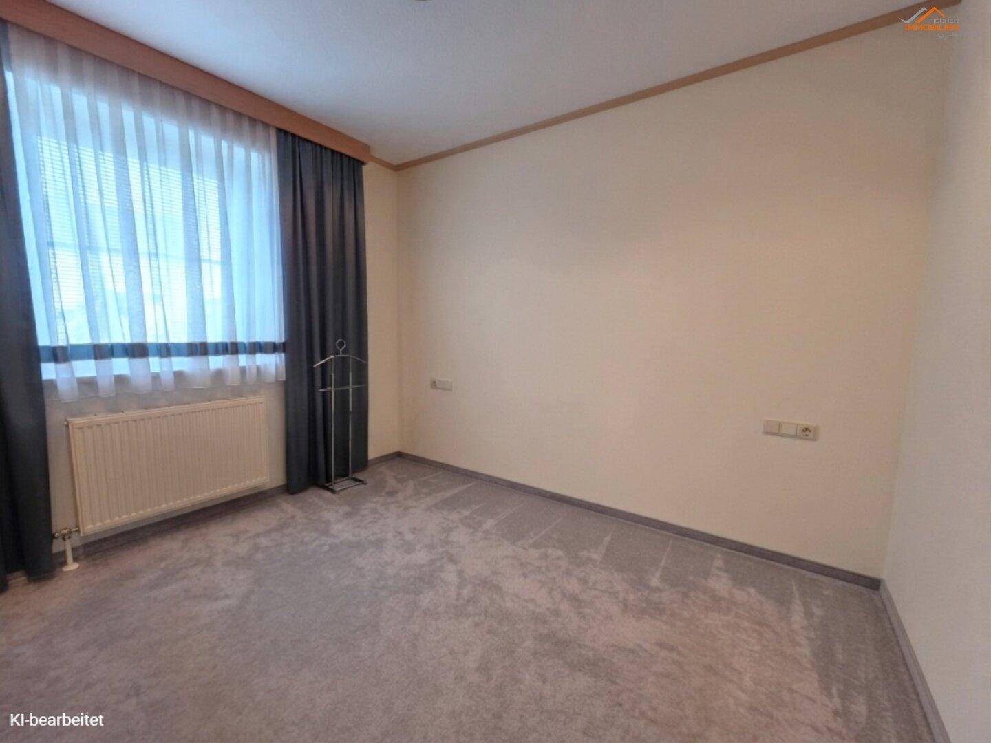 Schlafzimmer mit grauem Teppichboden, großem Fenster und einem Heizkörper.