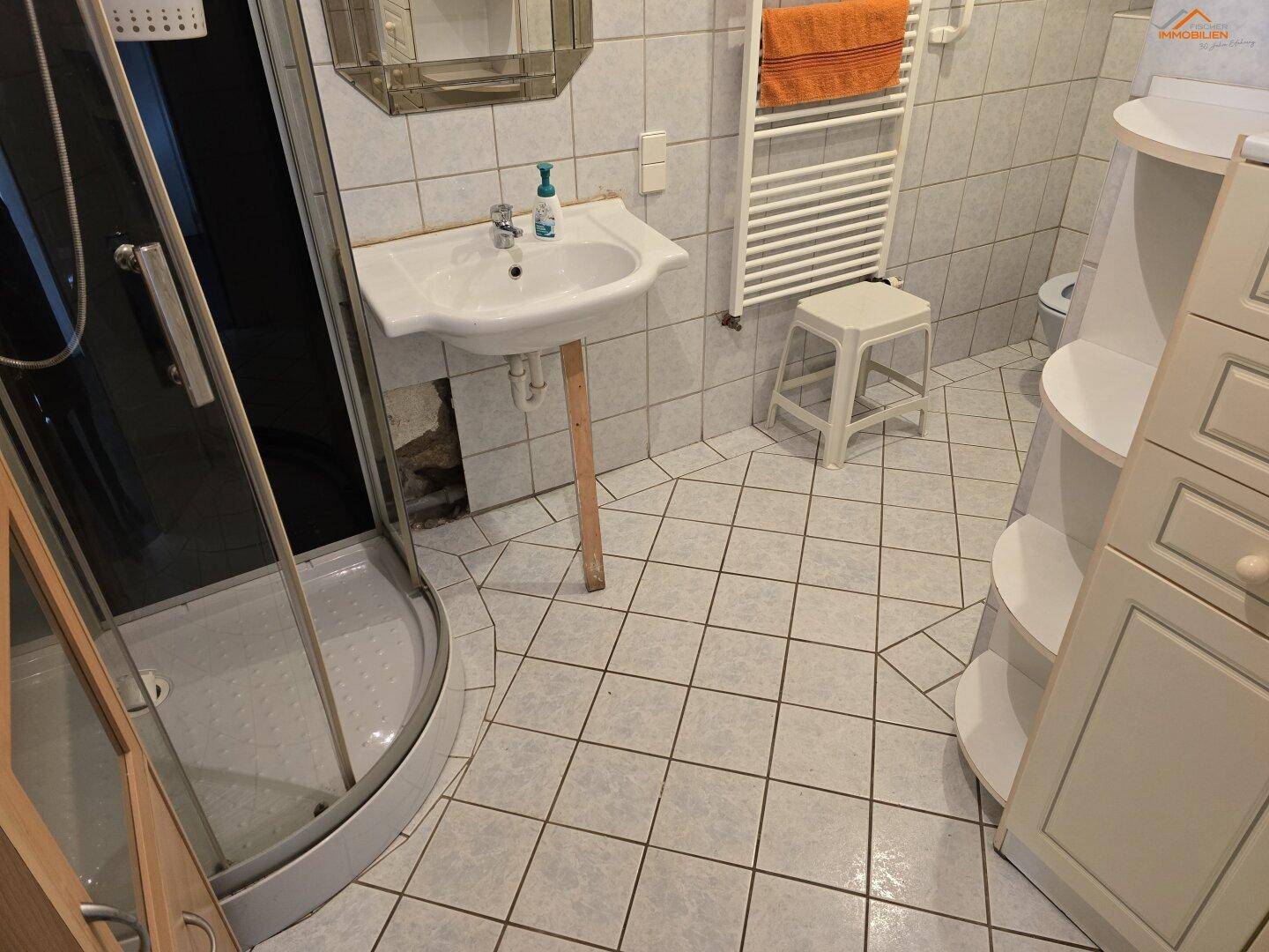 Badezimmer mit Duschkabine, Waschbecken und Fliesenboden in hellem Design.