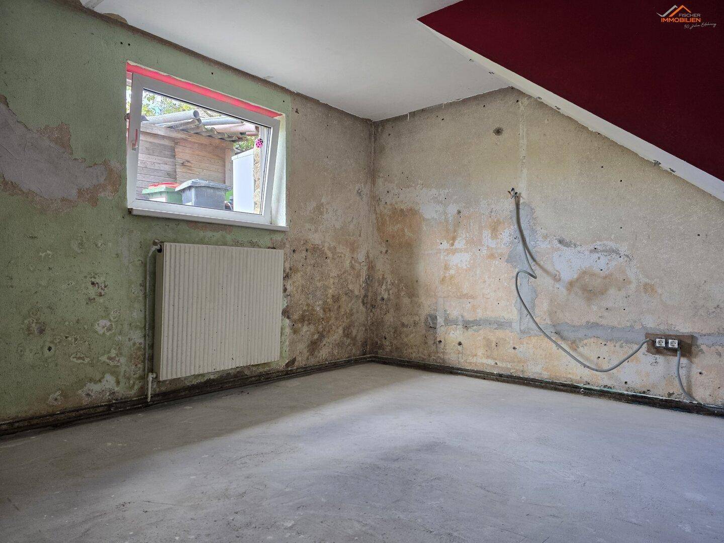 Unfertiger Raum mit schrägen Wänden, Fenster und Renovierungsbedarf.