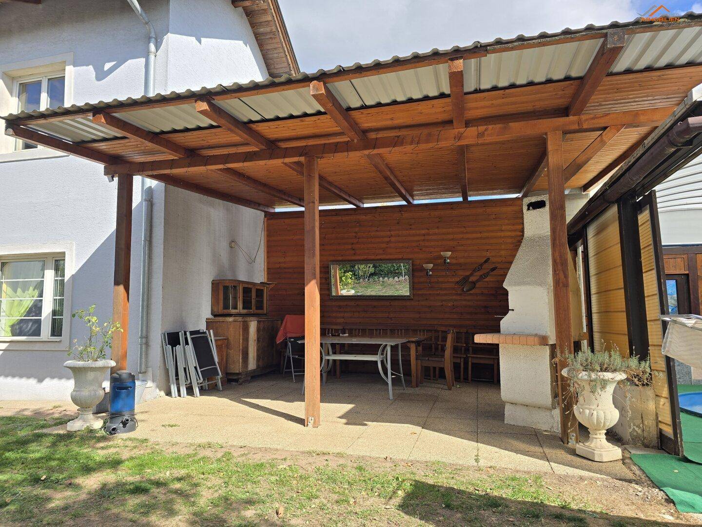 Überdachte Terrasse mit Essbereich, Grill und Blick in den Garten.