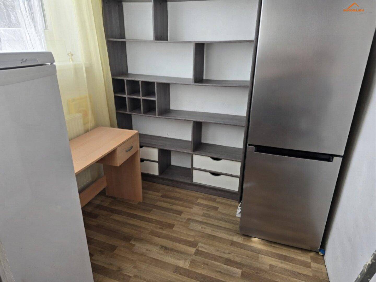 Kleiner Raum mit Kühlschrank, Regal und Schreibtisch, ideal als Abstellraum.