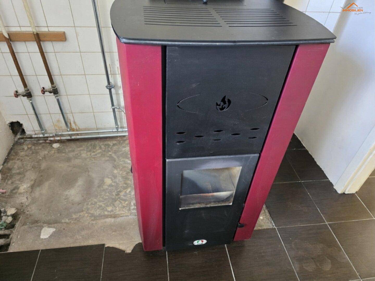 Heizraum mit Pelletsofen, Fliesenboden und sichtbaren Rohren.