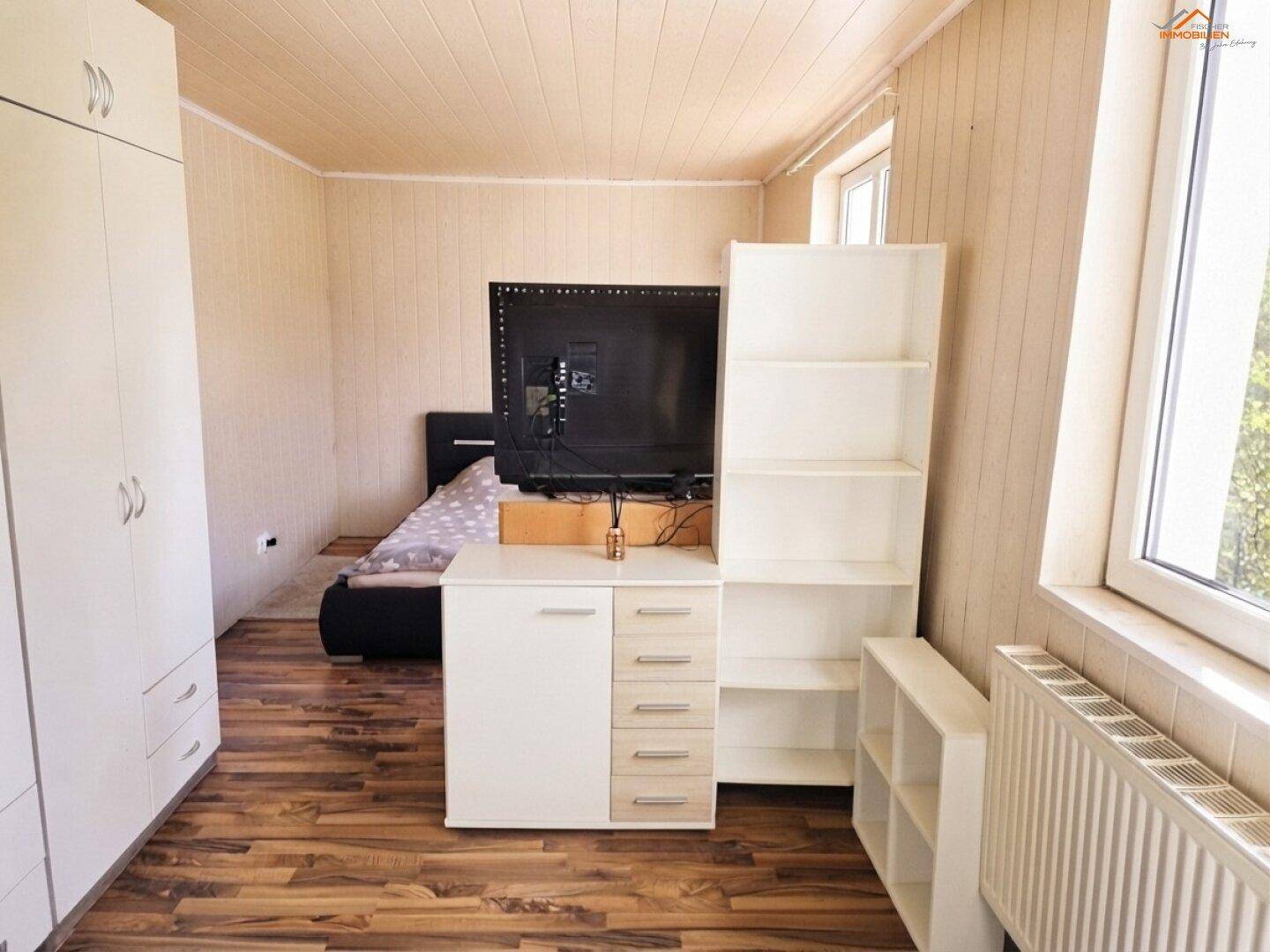 Schlafzimmer mit Holzwänden, Laminatboden und weißem Kleiderschrank.