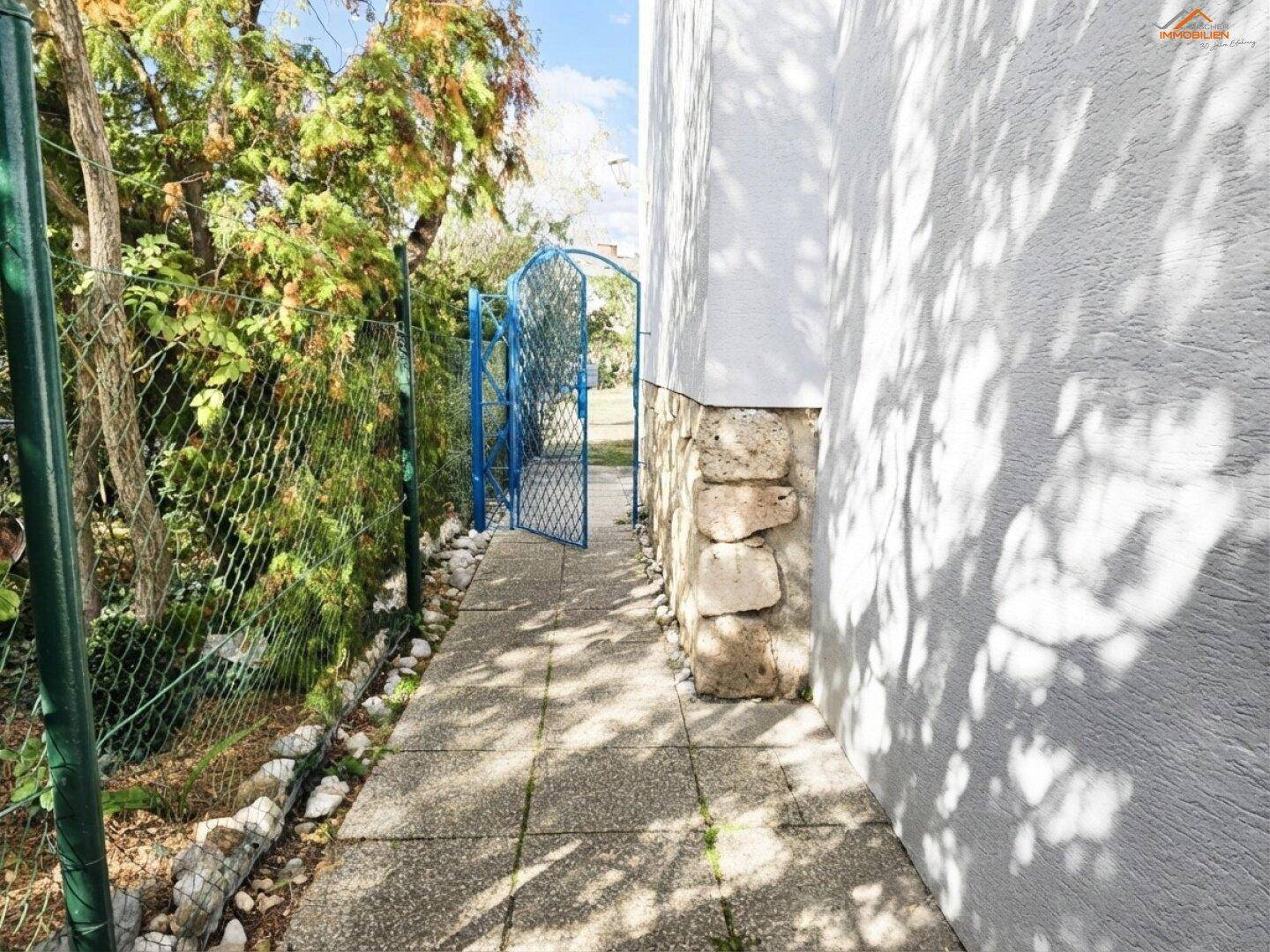 Seitenweg am Haus mit Zaun und blauem Gartentor.