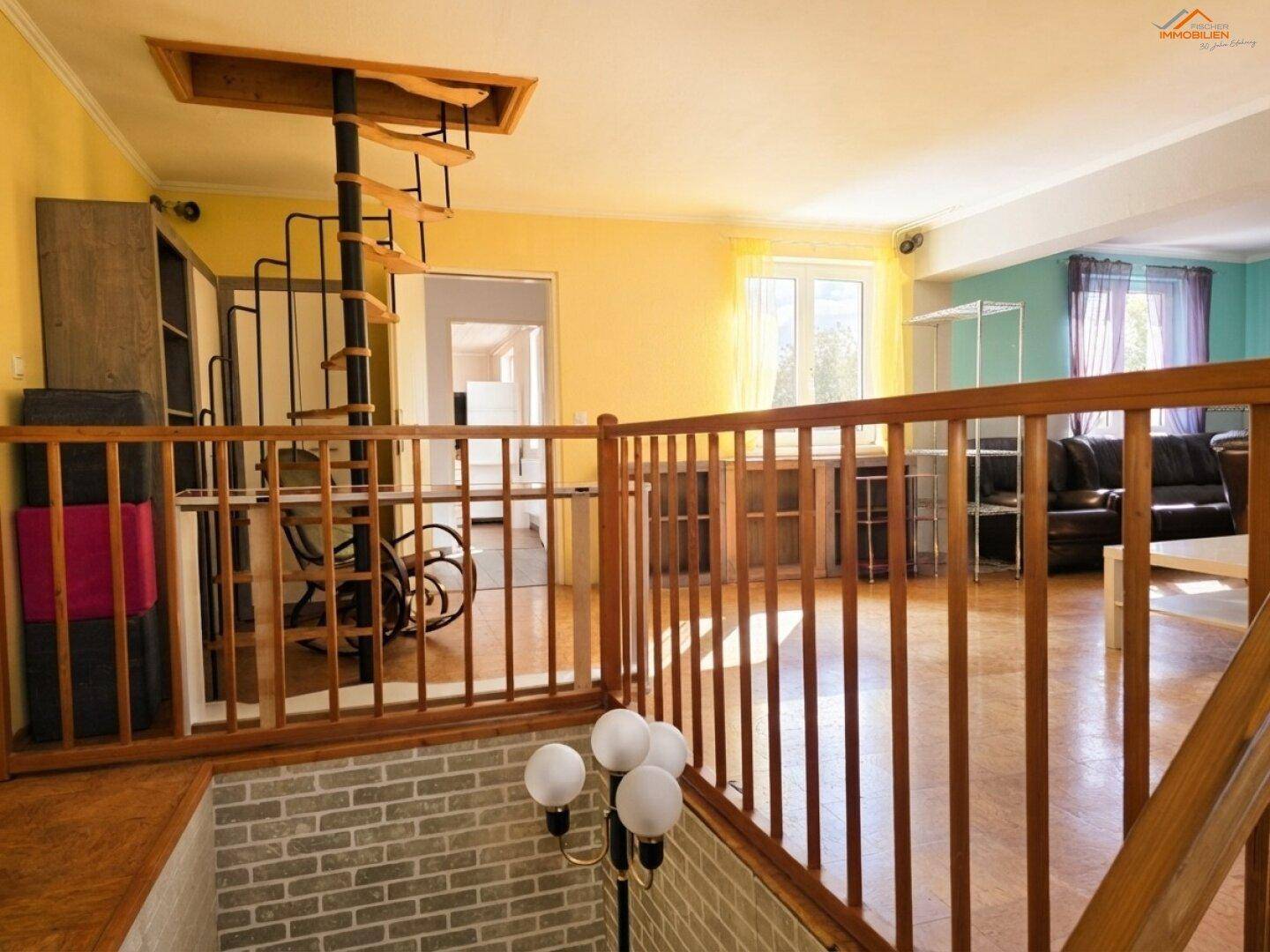 Geräumiges Wohnzimmer mit Holzgeländer, Wendeltreppe und hellem Parkettboden.