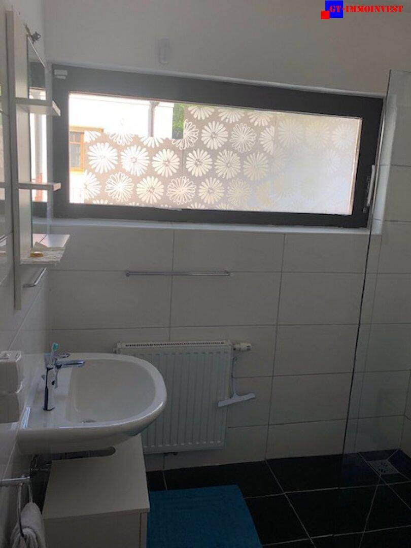 Badezimmer mit Waschbecken, Spiegelschrank, Heizkörper und Fenster mit Sichtschutzfolie.