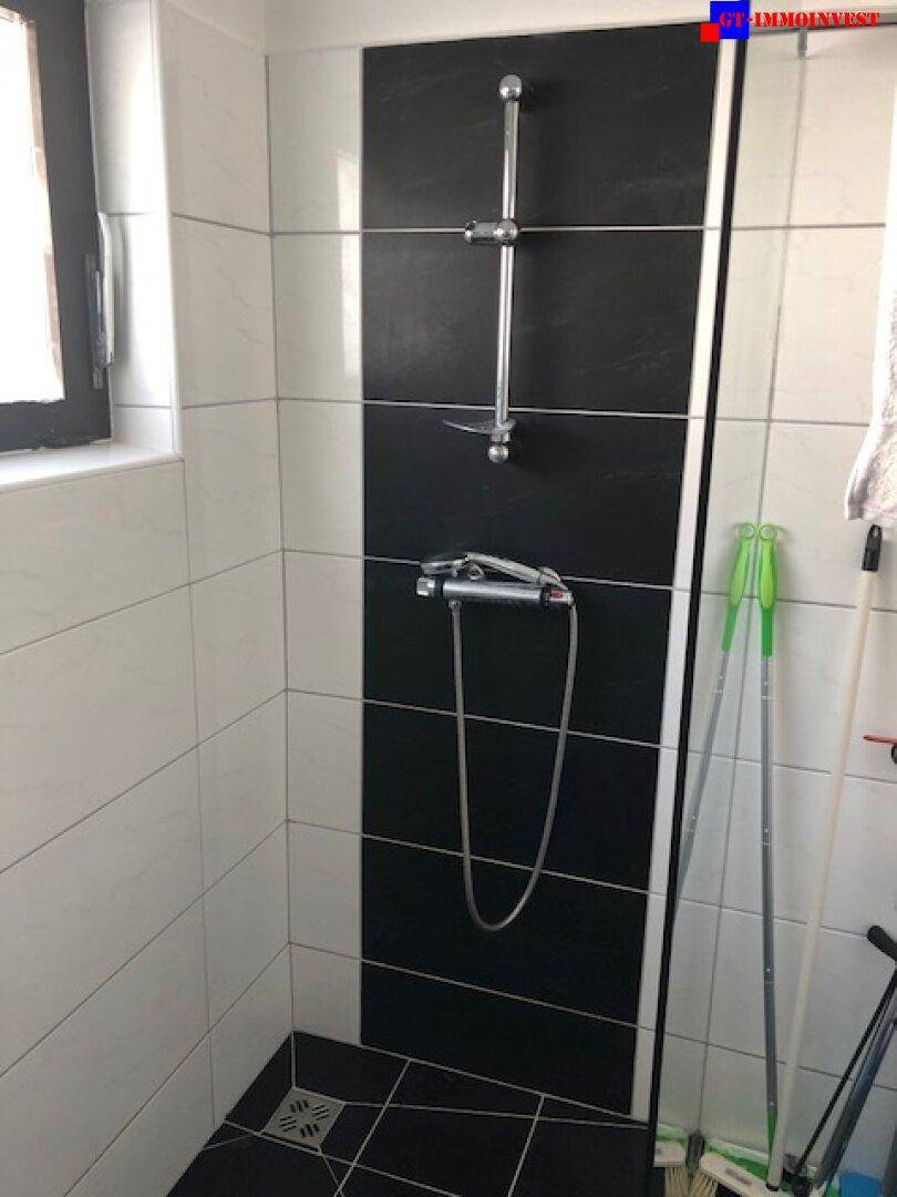 Duschbereich im Badezimmer mit modernen schwarz-weißen Fliesen und Duscharmatur.