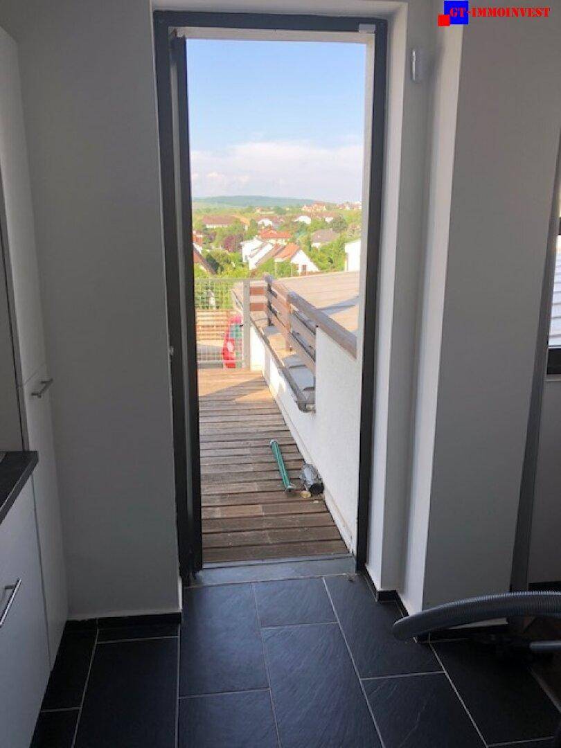 Blick durch eine offene Tür auf eine Holzterrasse mit weitreichender Aussicht über die Umgebung.