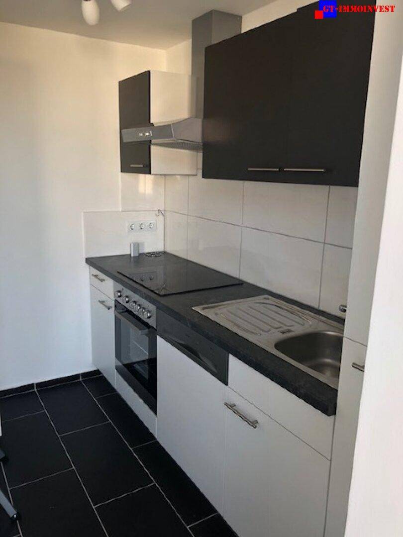 Kompakte Küche mit modernen schwarz-weißen Schränken, Induktionskochfeld und dunklem Fliesenboden.