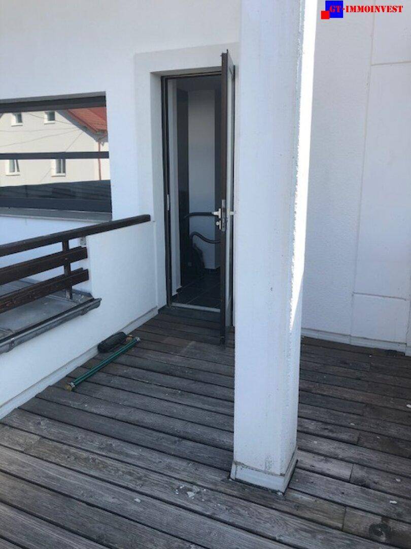 Geräumige Holzterrasse mit Zugang zu einem Innenraum und Blick auf die Umgebung.