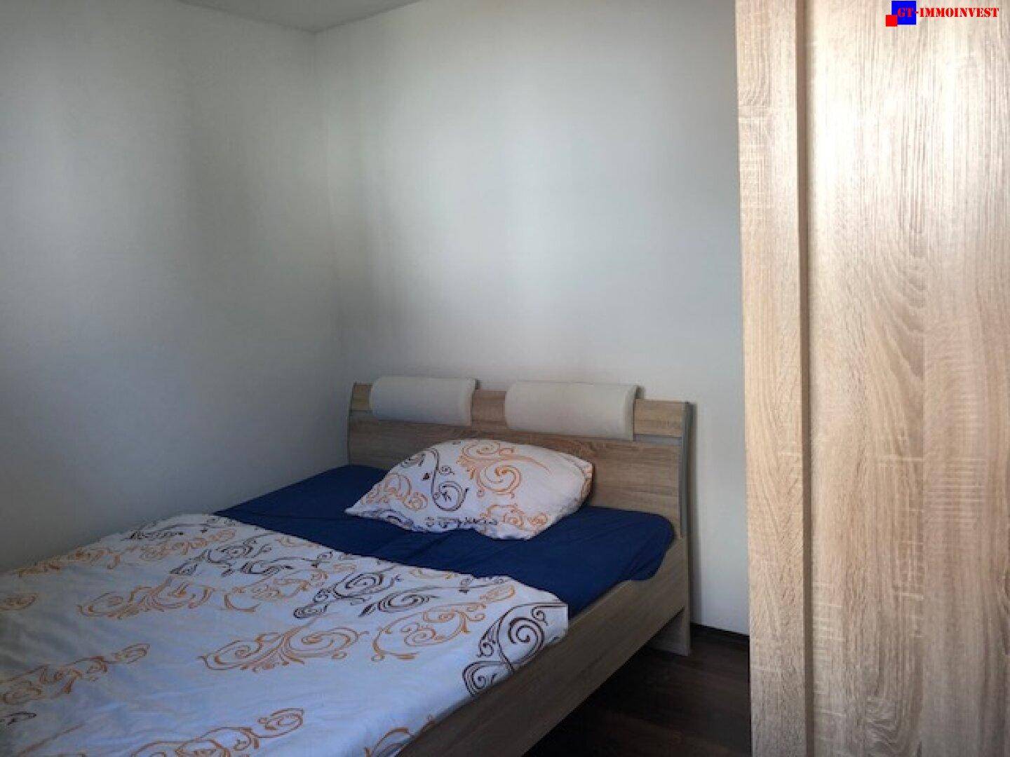 Schlafzimmer mit hellem Holzbett, gemusterter Bettwäsche und dunklem Boden.