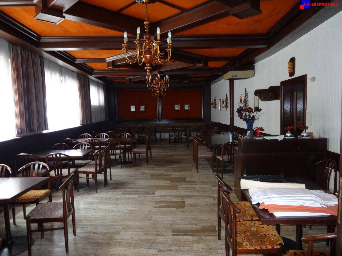 Geräumiger Speisesaal mit traditioneller Holzdecke, Kronleuchtern und zahlreichen Tischen und Stühlen.