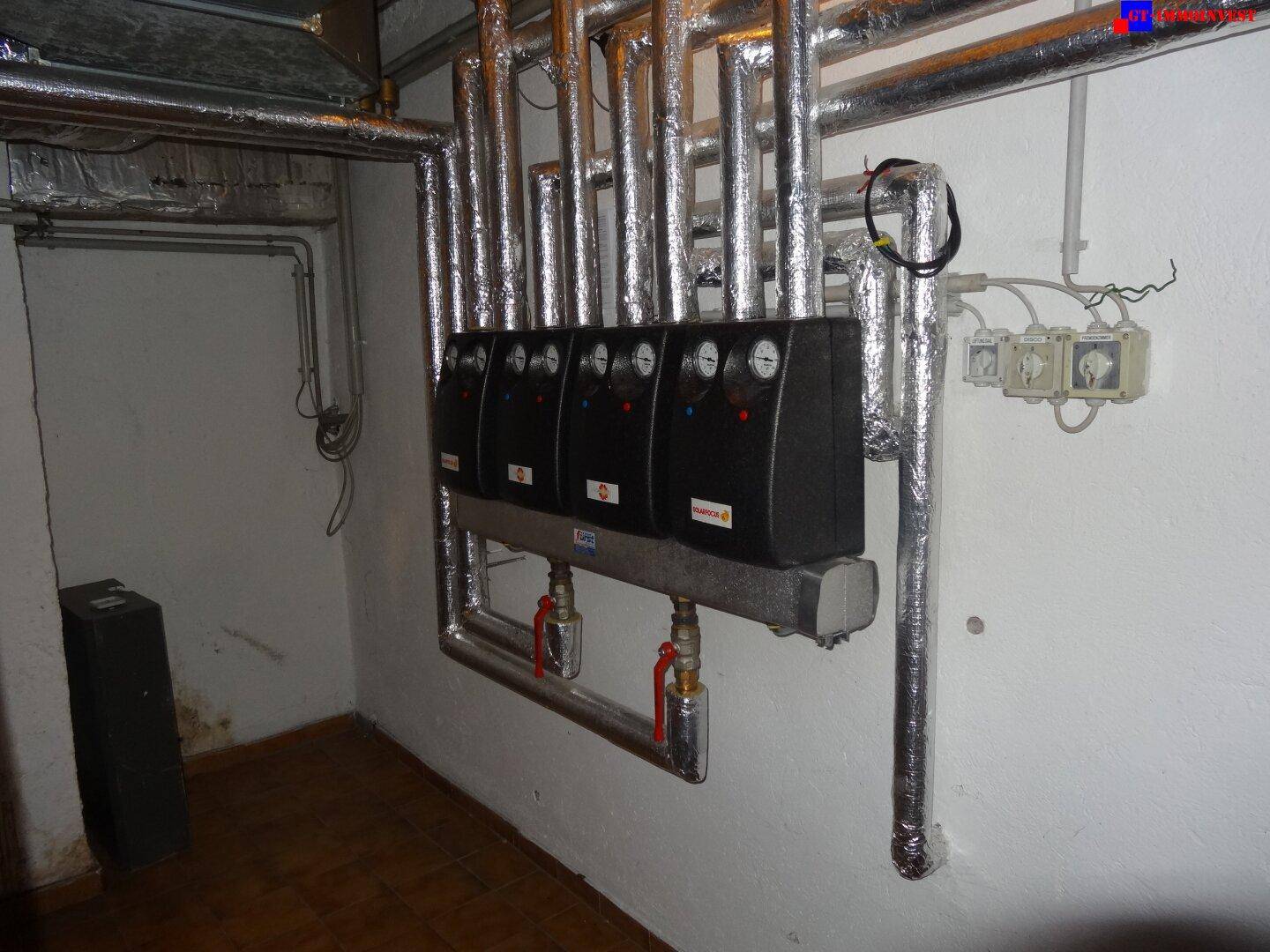 Technikraum oder Keller mit isolierten Rohren und Steuerungseinheiten an der Wand.