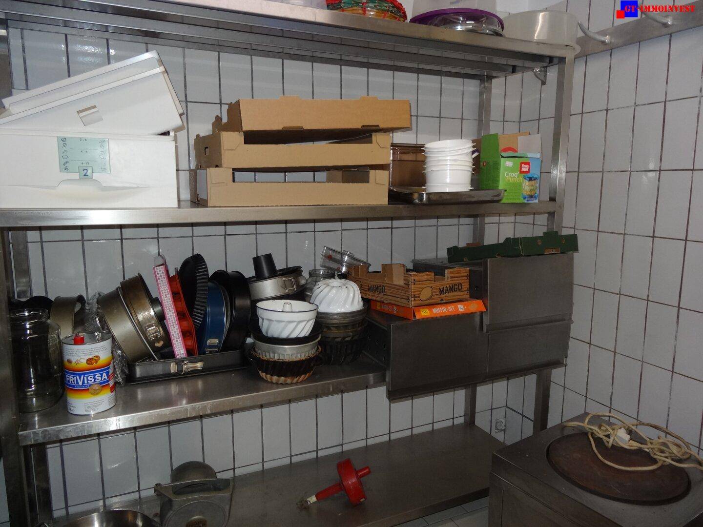 Lagerbereich mit Edelstahlregalen, gefliesten Wänden und verschiedenen Küchenutensilien.