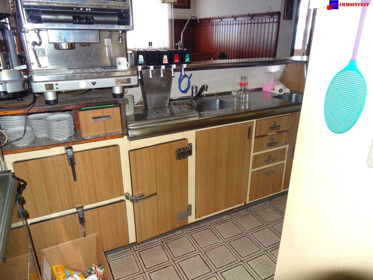 Kleine Küchenzeile oder Servicebereich mit Kaffeemaschine, Spüle und einfachen Holzschränken.