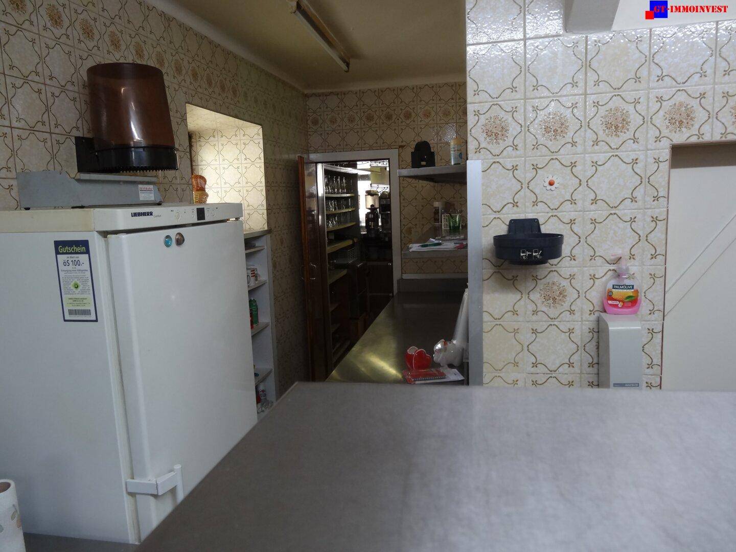 Teil einer Großküche oder eines Lagerbereichs mit großem Kühlschrank und gemusterten Fliesen an den Wänden.