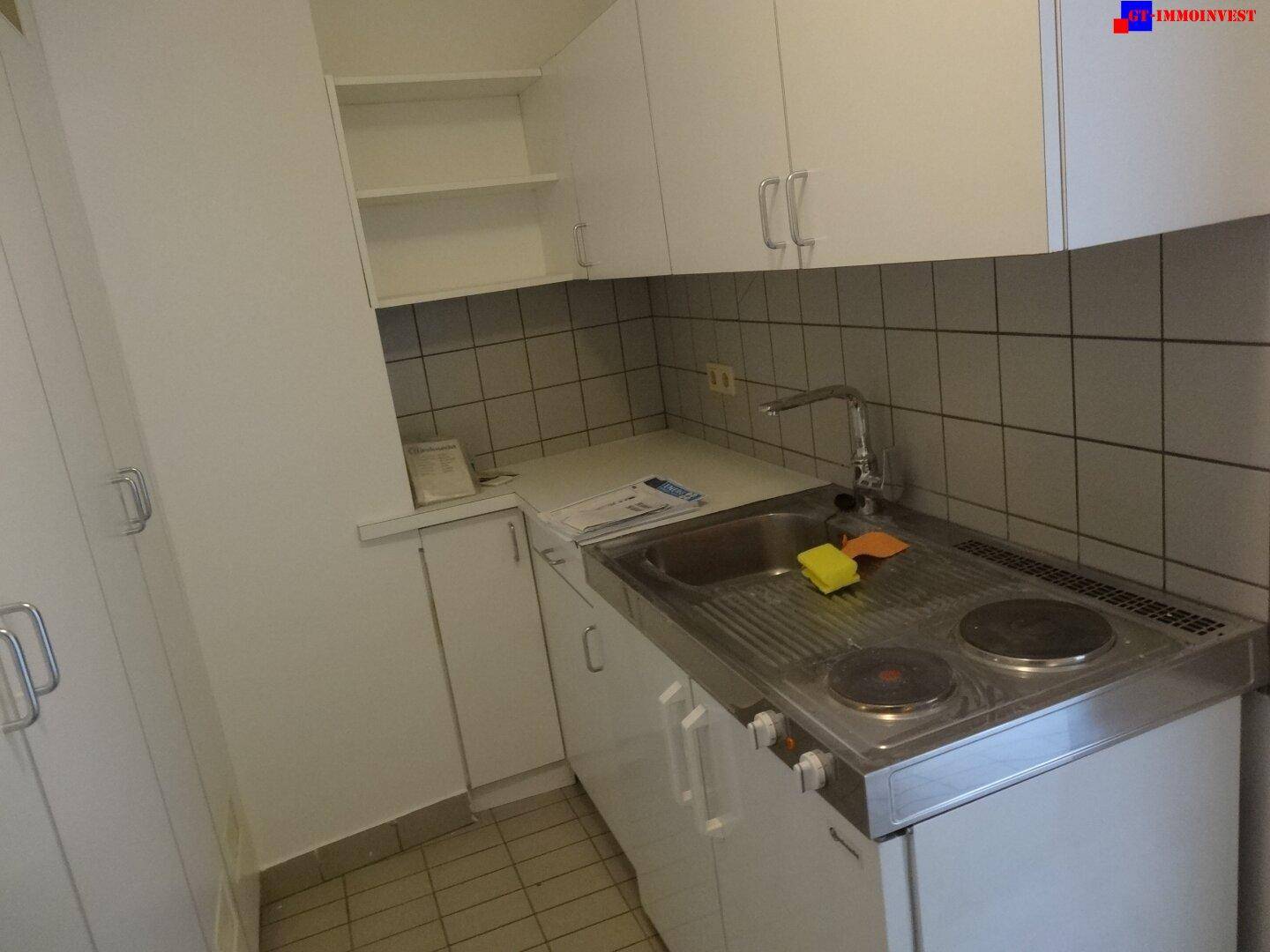 Kompakte Küchenzeile mit weißen Schränken, Spüle und zwei Kochplatten, ideal für kleine Wohnungen.