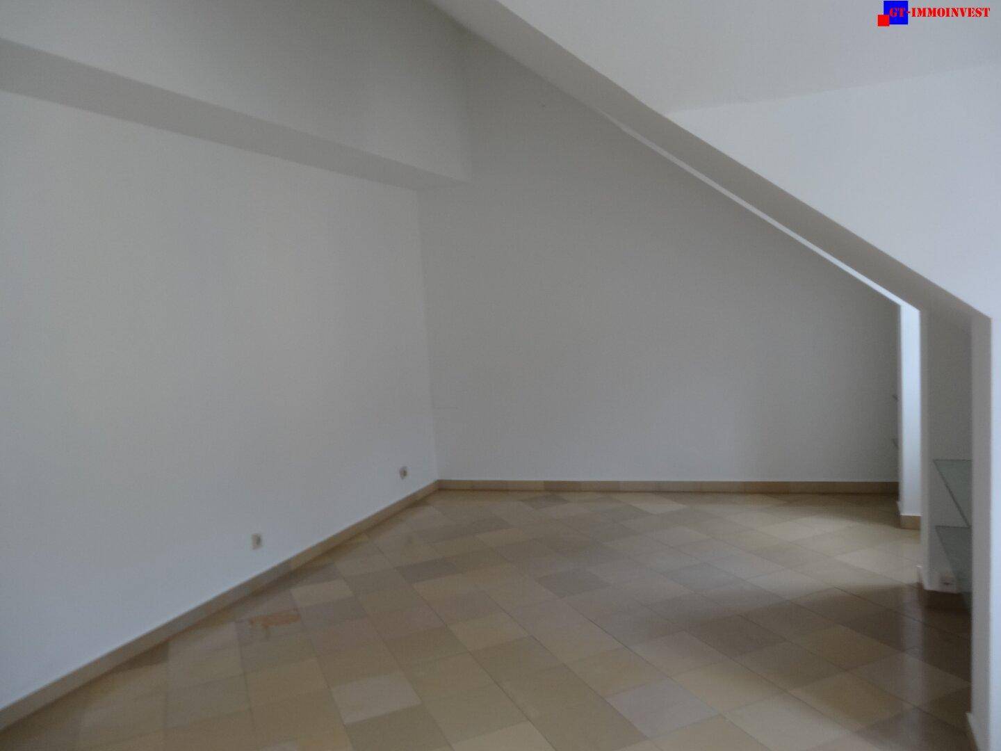 Leerer Wohnbereich mit schrägen Wänden und hellen Fliesenböden, der auf eine zukünftige Gestaltung wartet.