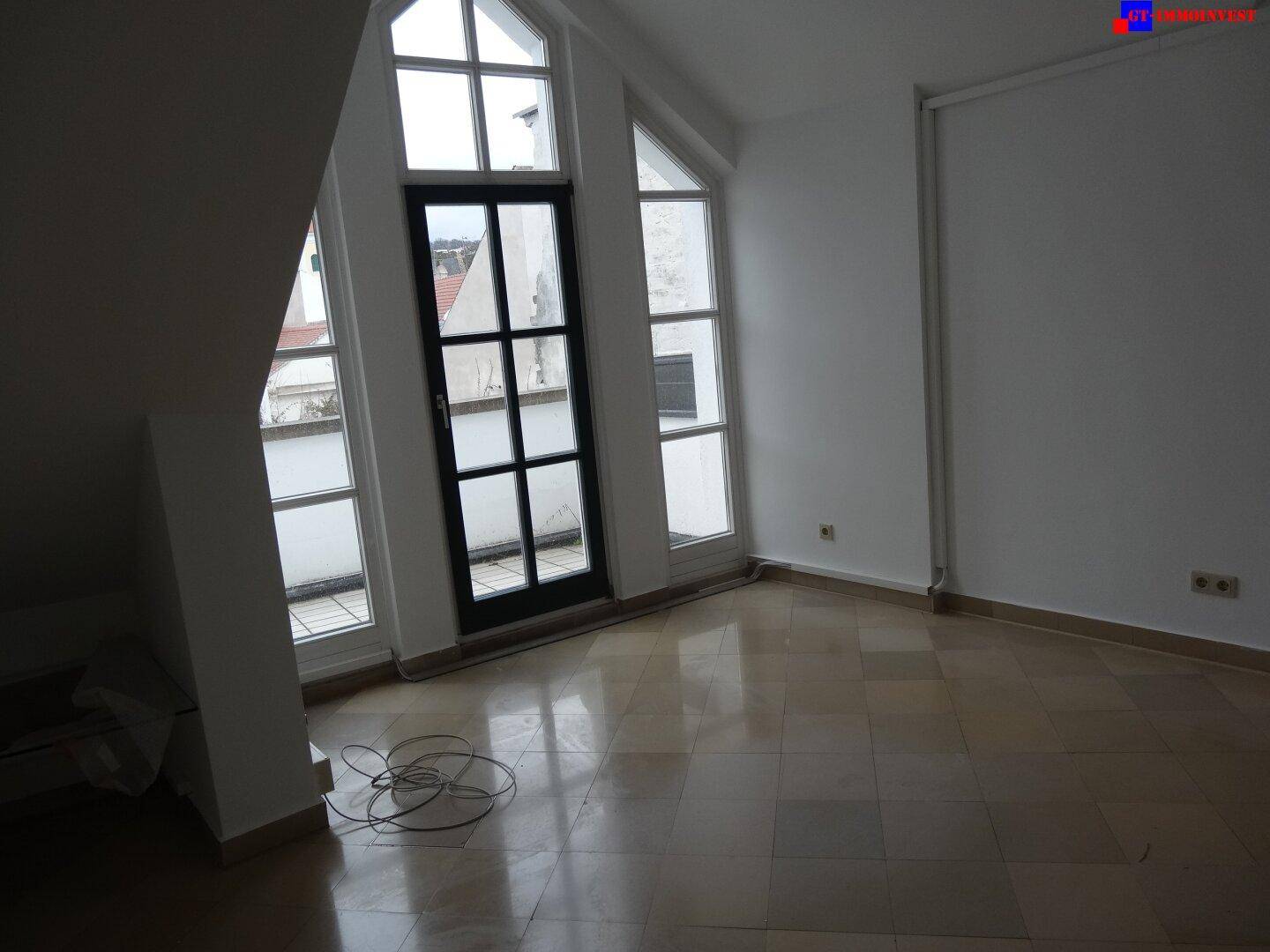 Offener Wohnbereich mit Zugang zu einem Außenbereich durch eine große Glastür und hohen Fenstern.