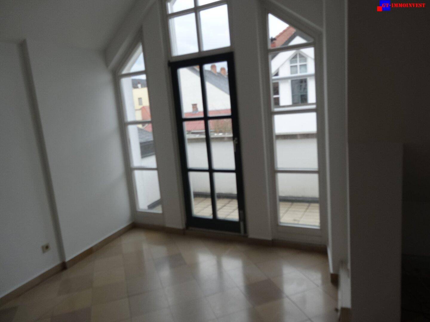 Heller Wohnbereich mit Zugang zu einem Außenbereich durch eine hohe Glastür und seitliche Fenster.