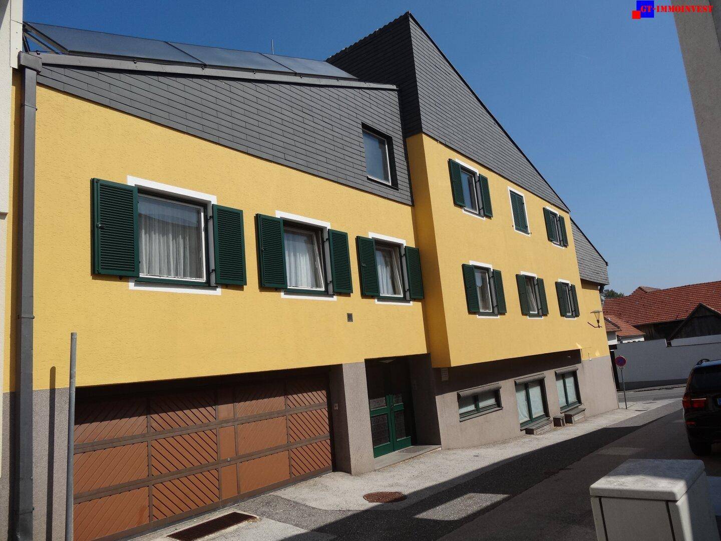 Seitenansicht des gelben Gebäudes mit dunklen Fensterläden und Garagentor.