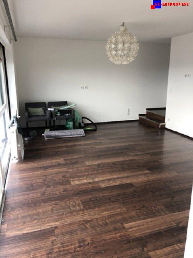 Heller Wohnbereich mit dunklem Holzboden und Blick auf die Treppe zu einer oberen Etage.