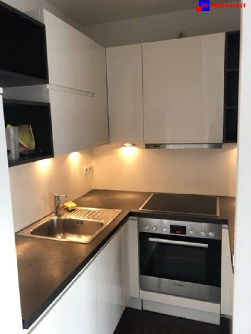 Moderne, kompakte Küchenzeile mit weißen Hochglanzschränken, integriertem Backofen und Kochfeld.