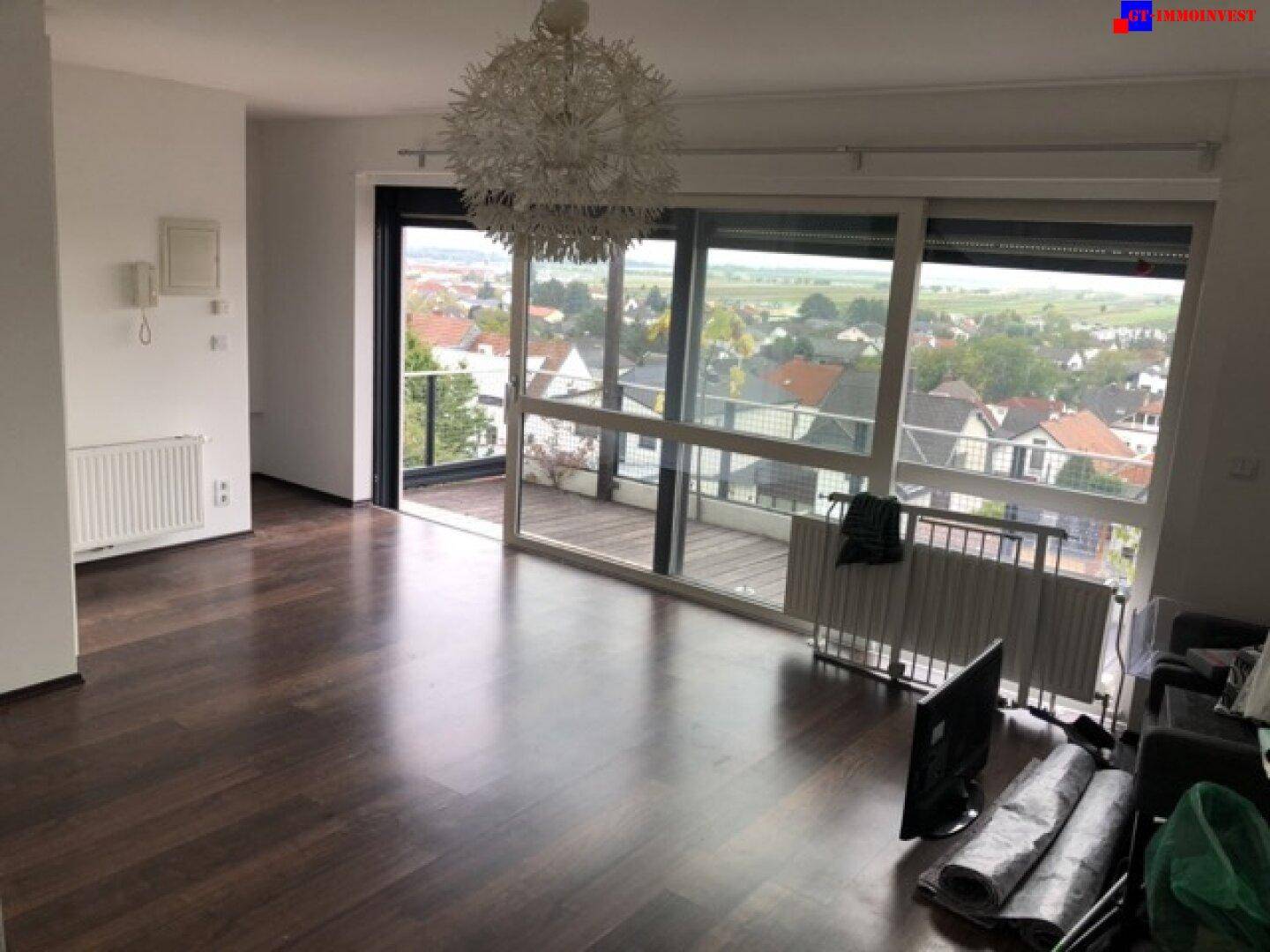Geräumiges Wohnzimmer mit dunklem Holzboden, viel Tageslicht und Zugang zur Außenterrasse.