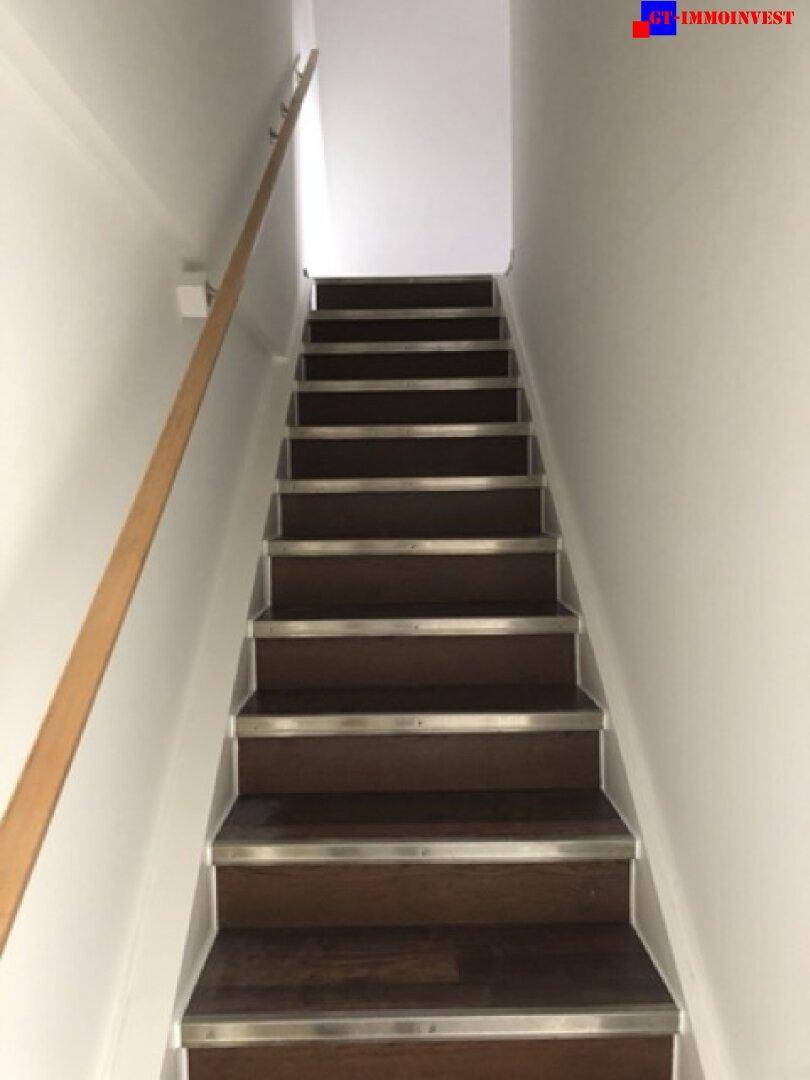 Holztreppe mit dunklen Stufen und hellem Handlauf, die in die obere Etage führt.