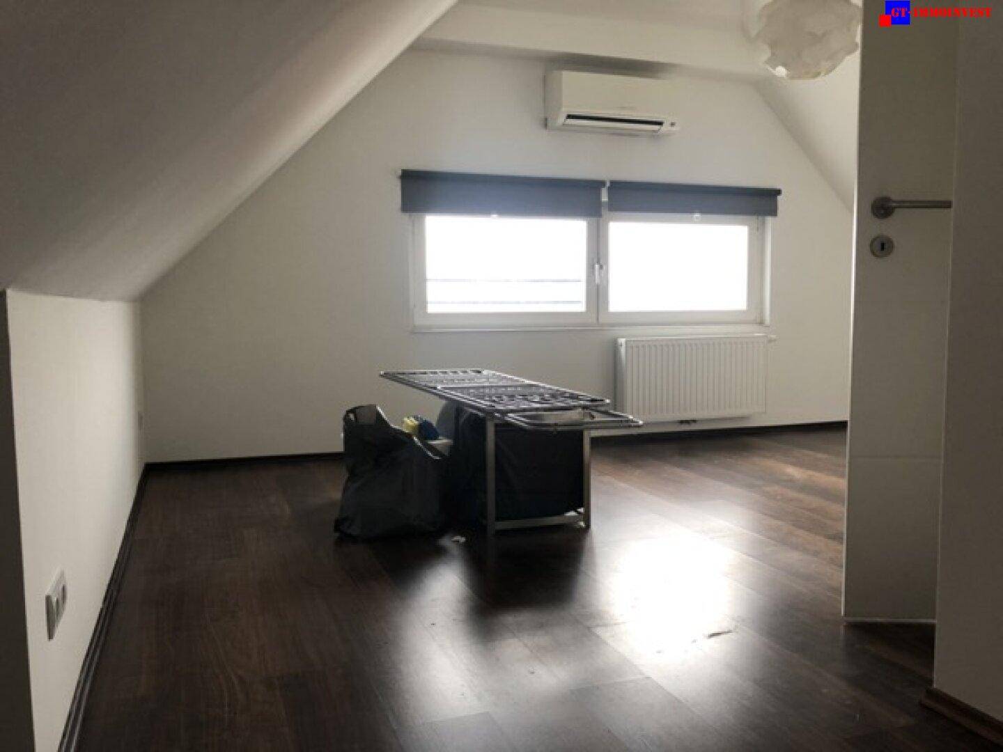 Dachgeschosszimmer mit dunklem Holzboden, Schrägdach und Klimaanlage an der Wand.