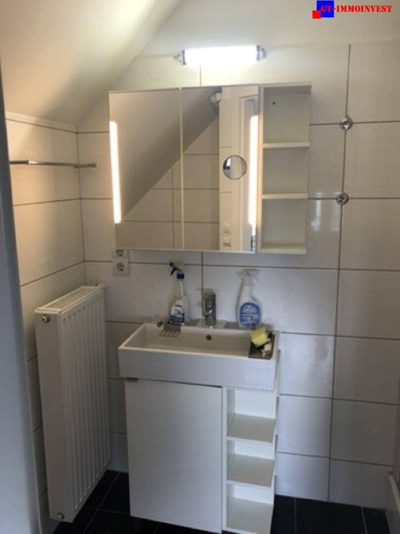 Badezimmer im Dachgeschoss mit Waschbecken, Spiegelschrank und weißen Wandfliesen.