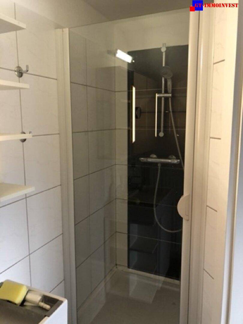 Moderne Duschkabine mit Glaswand und dunkler Rückwand in einem gefliesten Badezimmer.