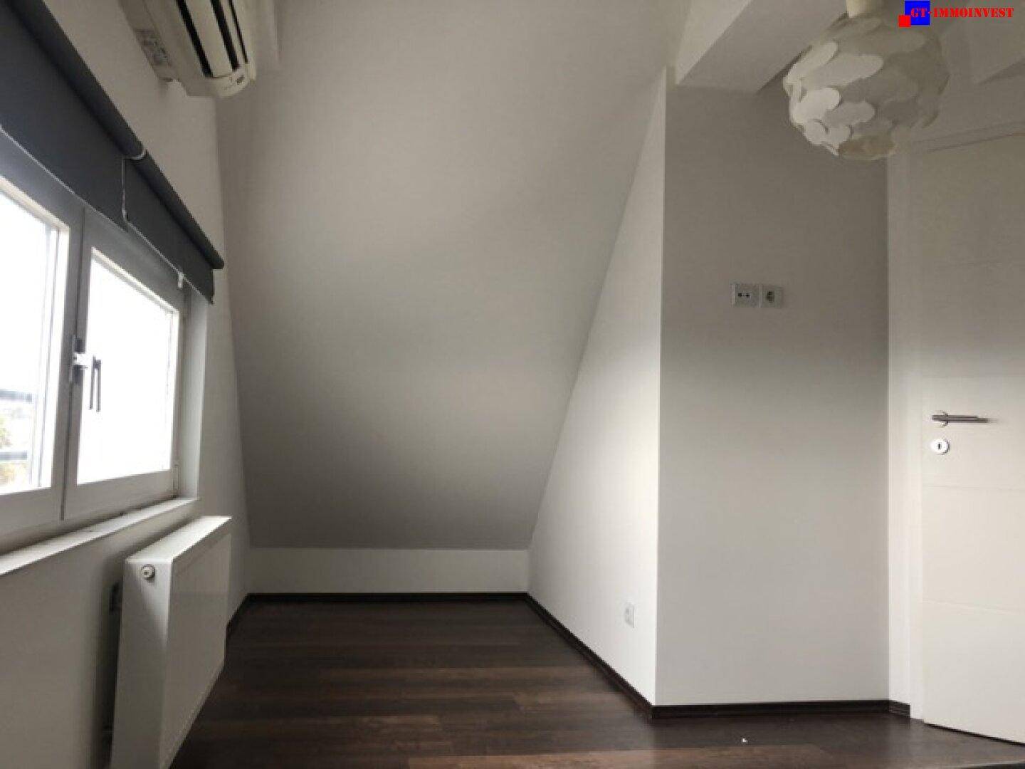 Helles Dachgeschosszimmer mit schrägen Wänden, dunklem Holzboden und Fenster für Tageslicht.