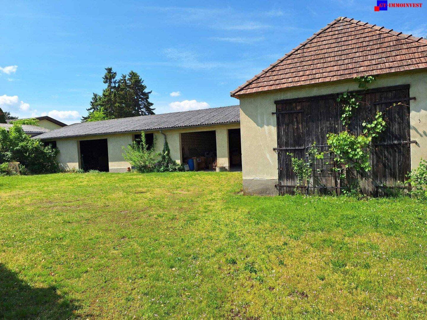 Weitläufige Rasenfläche vor einem langen Garagengebäude und einem Haus mit Ziegeldach unter klarem Himmel.