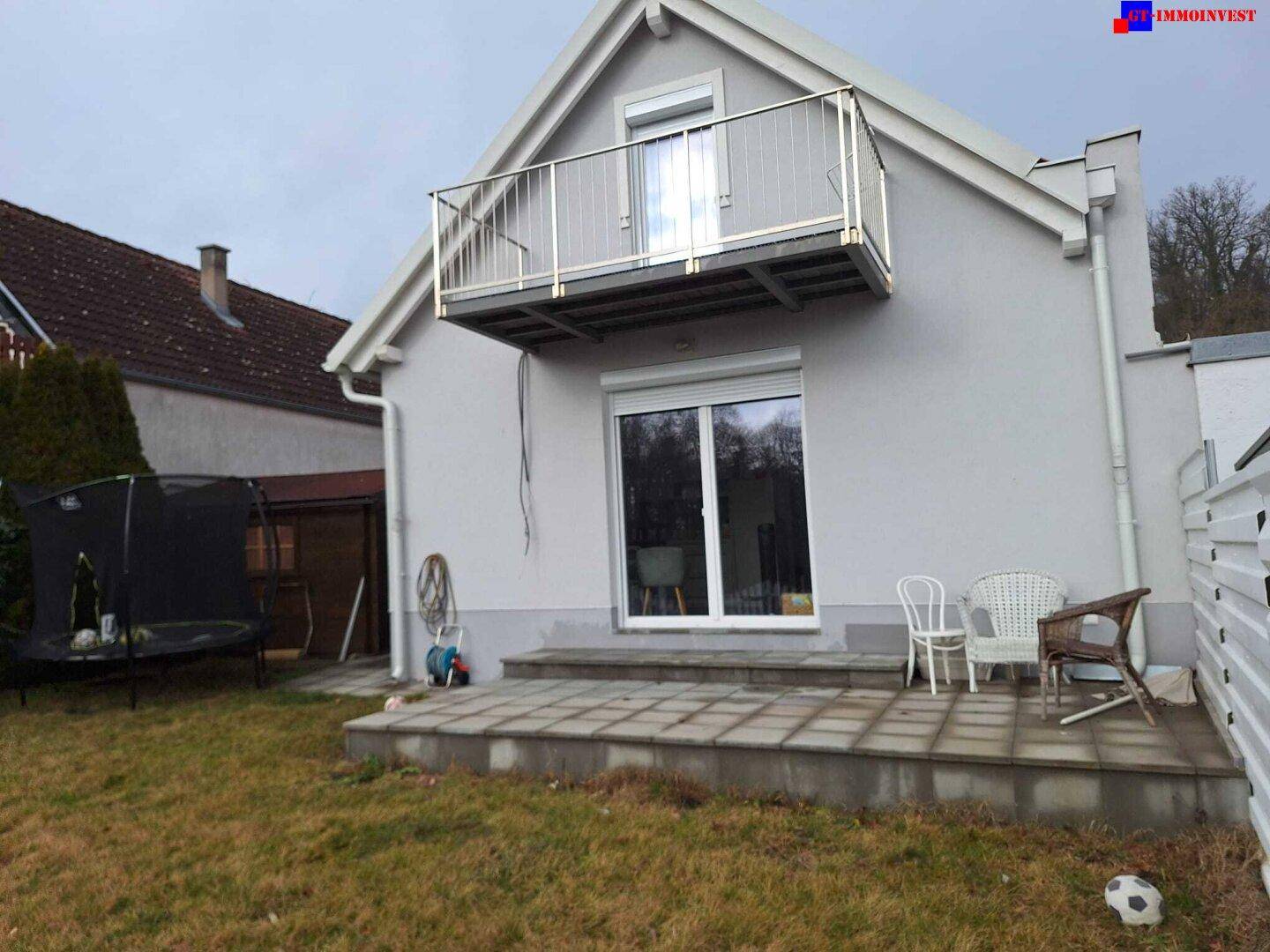 Rückansicht des Hauses mit Balkon, Terrasse, Garten und einem Trampolin.