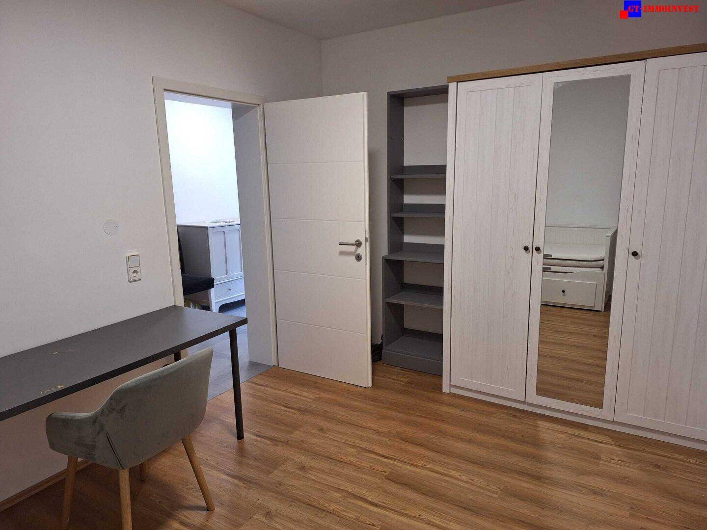 Schlafzimmer oder Arbeitszimmer mit Kleiderschrank, Schreibtisch und Laminatboden.